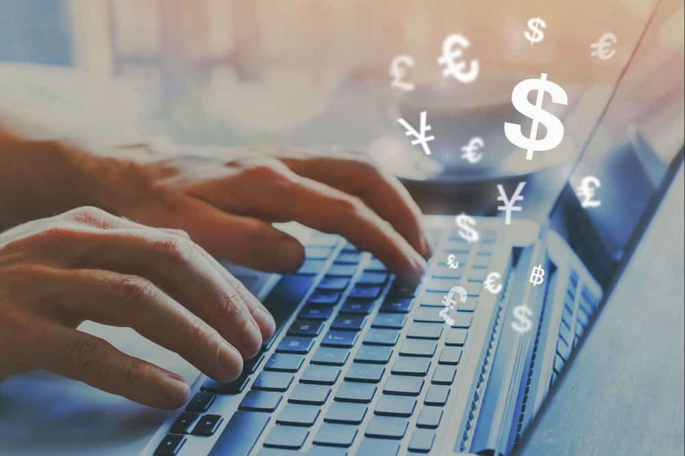 A person typing on a laptop with different currency symbols floating above the keyboard.